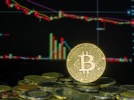 Gold Bitcoin coin standing on a pile of coins in front of a price chart